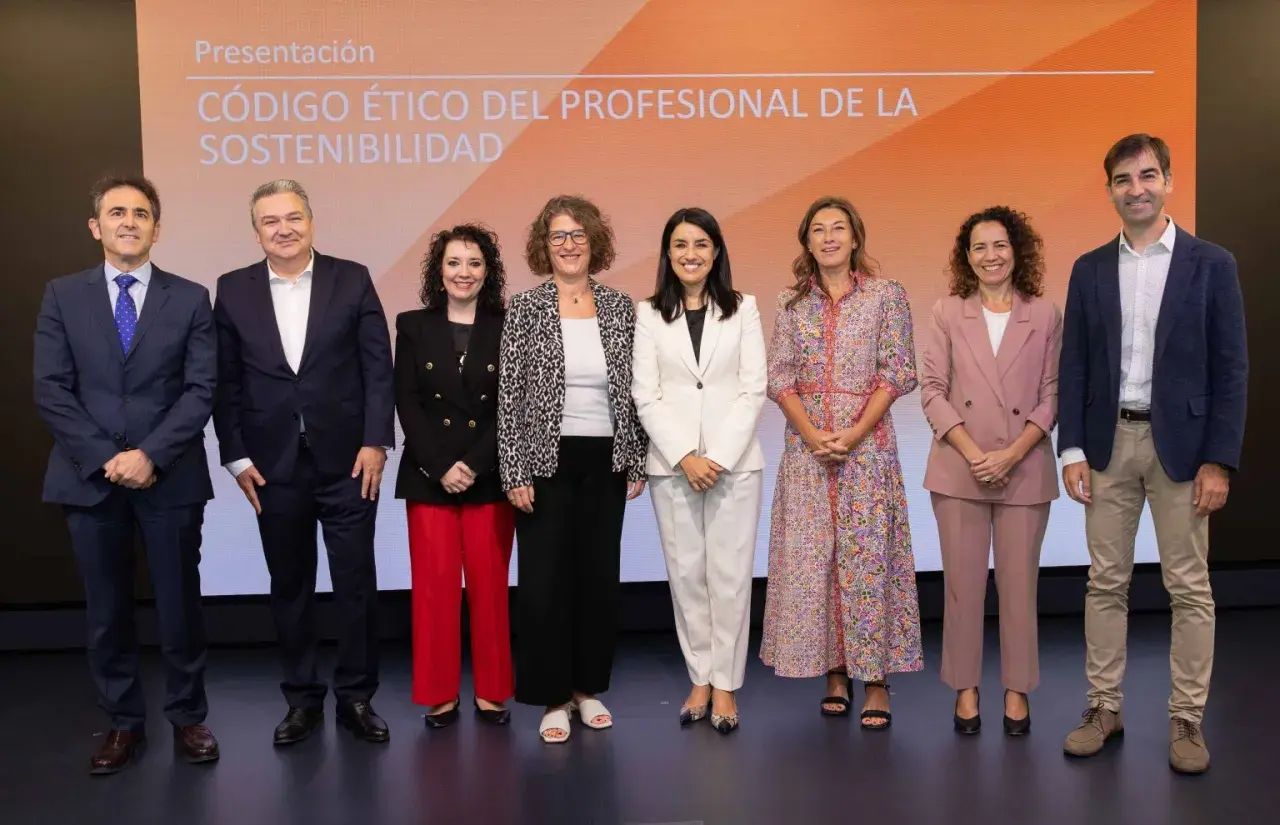Presentación del código de ética de una empresa. Un grupo de siete profesionales posa en un escenario con un fondo naranja y blanco.